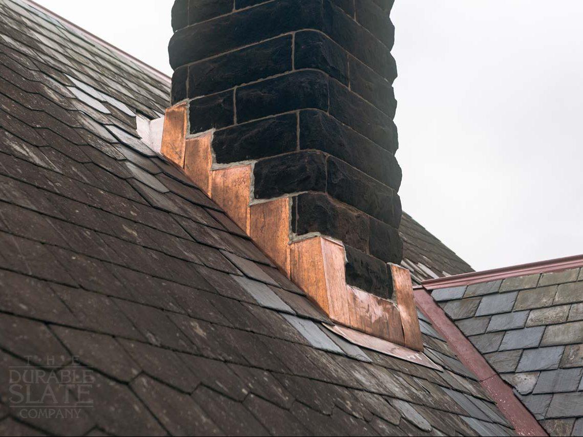 widok stromego dachu z kominem obudowanym czerwonymi dachówkami kominowymi w słońcu