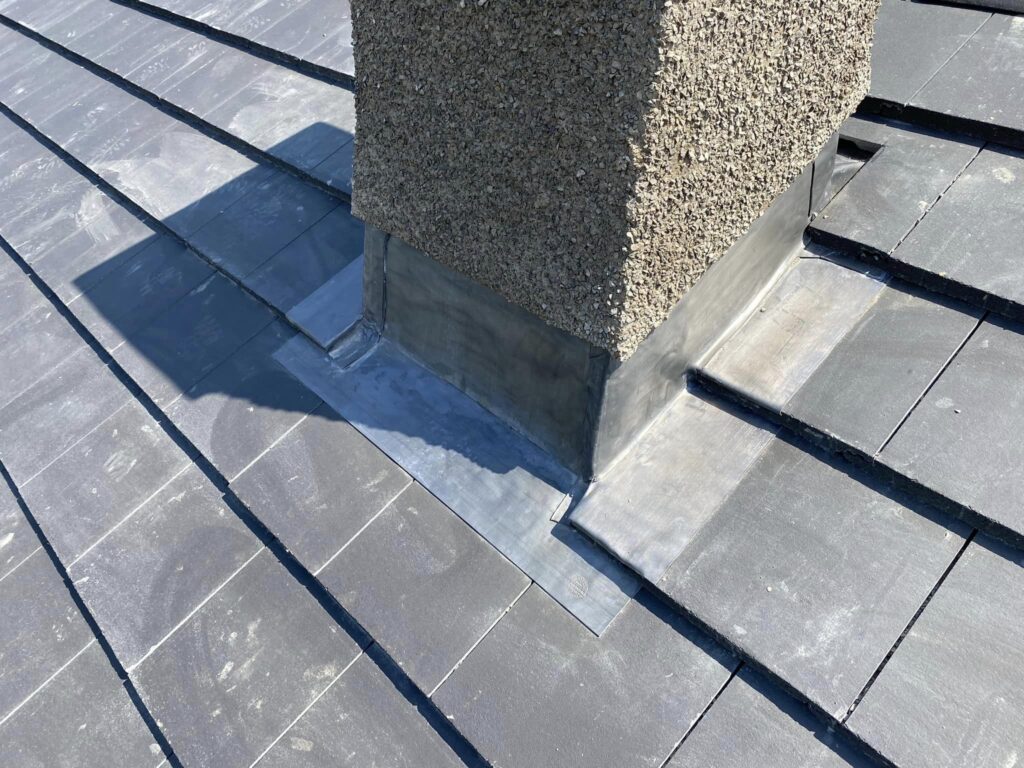 montaż dachówki kominowej na kominie robotnik w kasku układający dachówki kominowe wokół murowanego komina na dachu